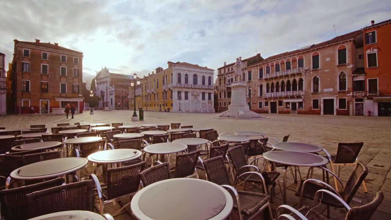 Bar all’aperto senza gente sulla piazza con edifici colorati