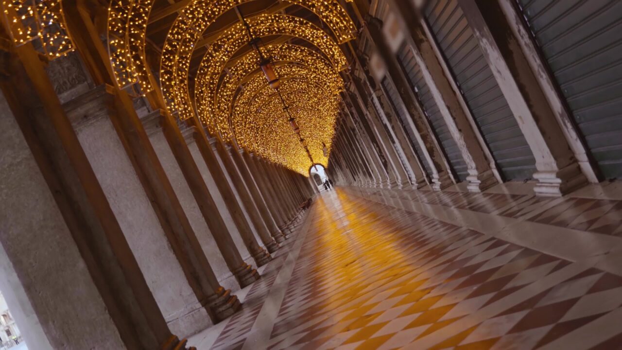 Movement under the arcades of a long building in Venice with Christmas lights