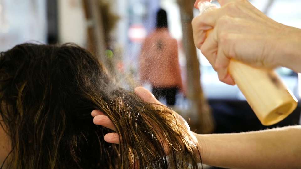 Spray is applied to the wet hair of the lady by the hairdresser