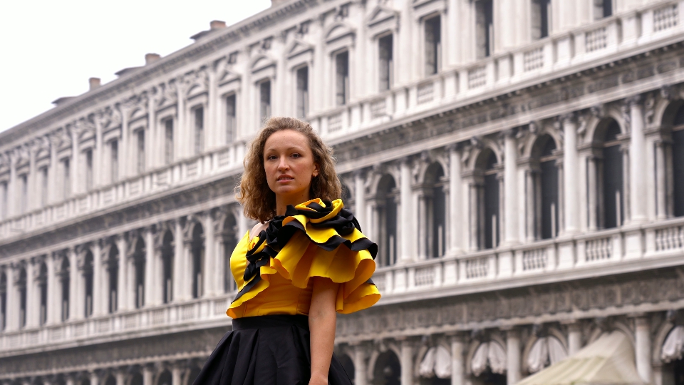 Woman in designer carnival dress poses against empty square