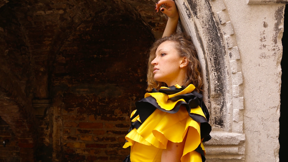 Young model in carnival dress leans on old antique arch