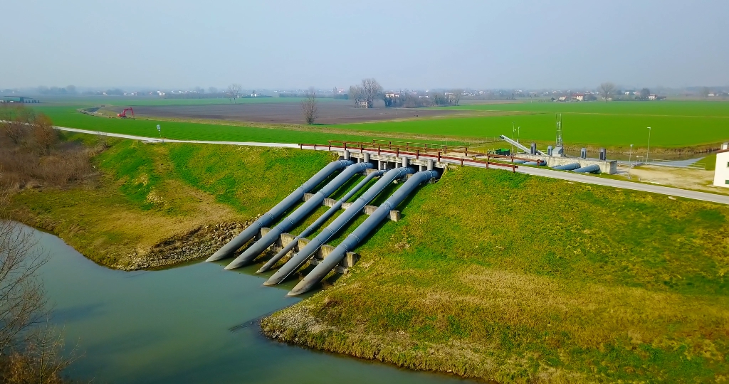 Road bridge over water supply system pipes on river by field