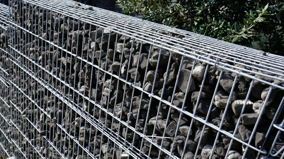 Designed fence with grey stones in metal grid cage in spring