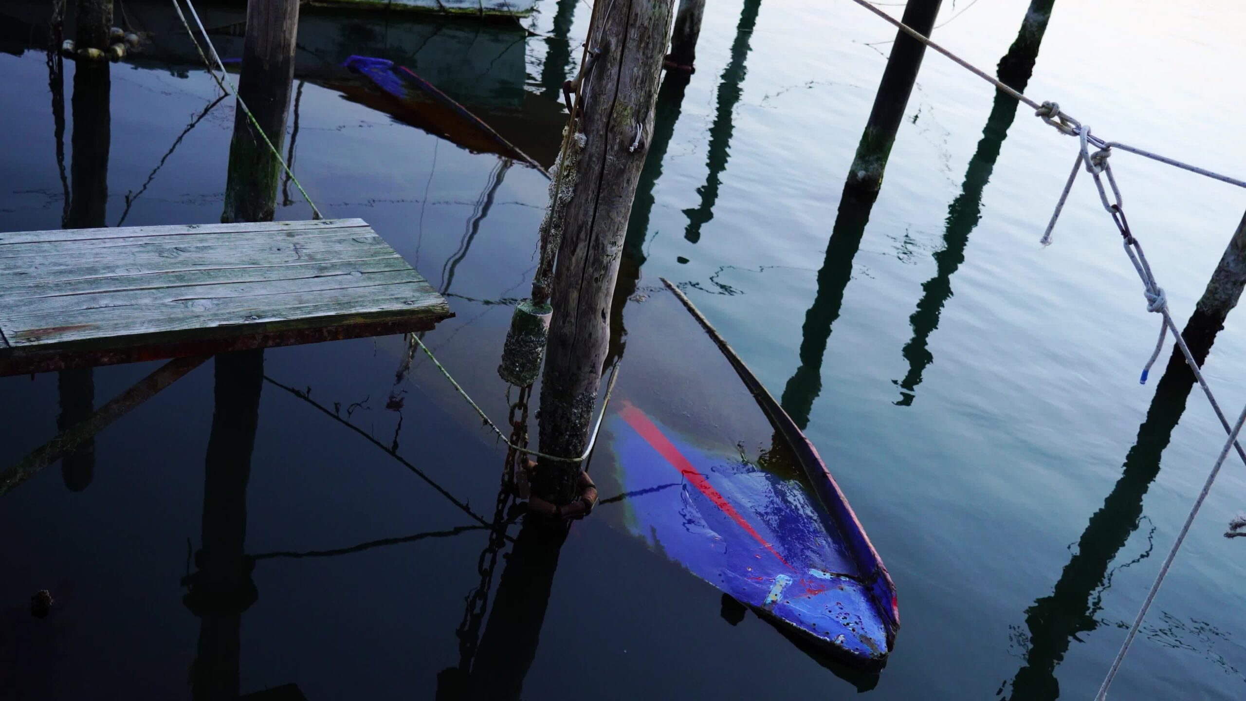 Large sunken boat carcass near moored wooden motorboats