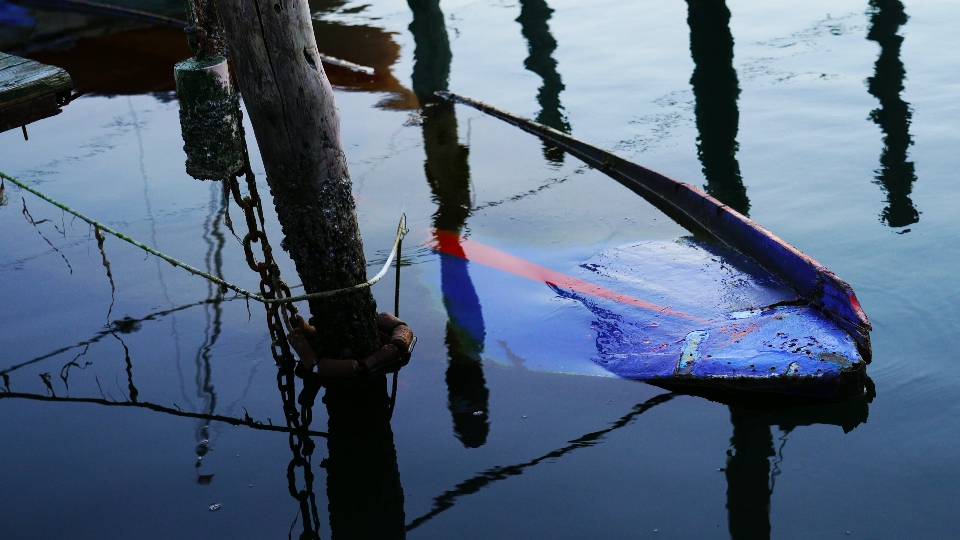 Broken boat drifts under lagoon surface among mooring poles