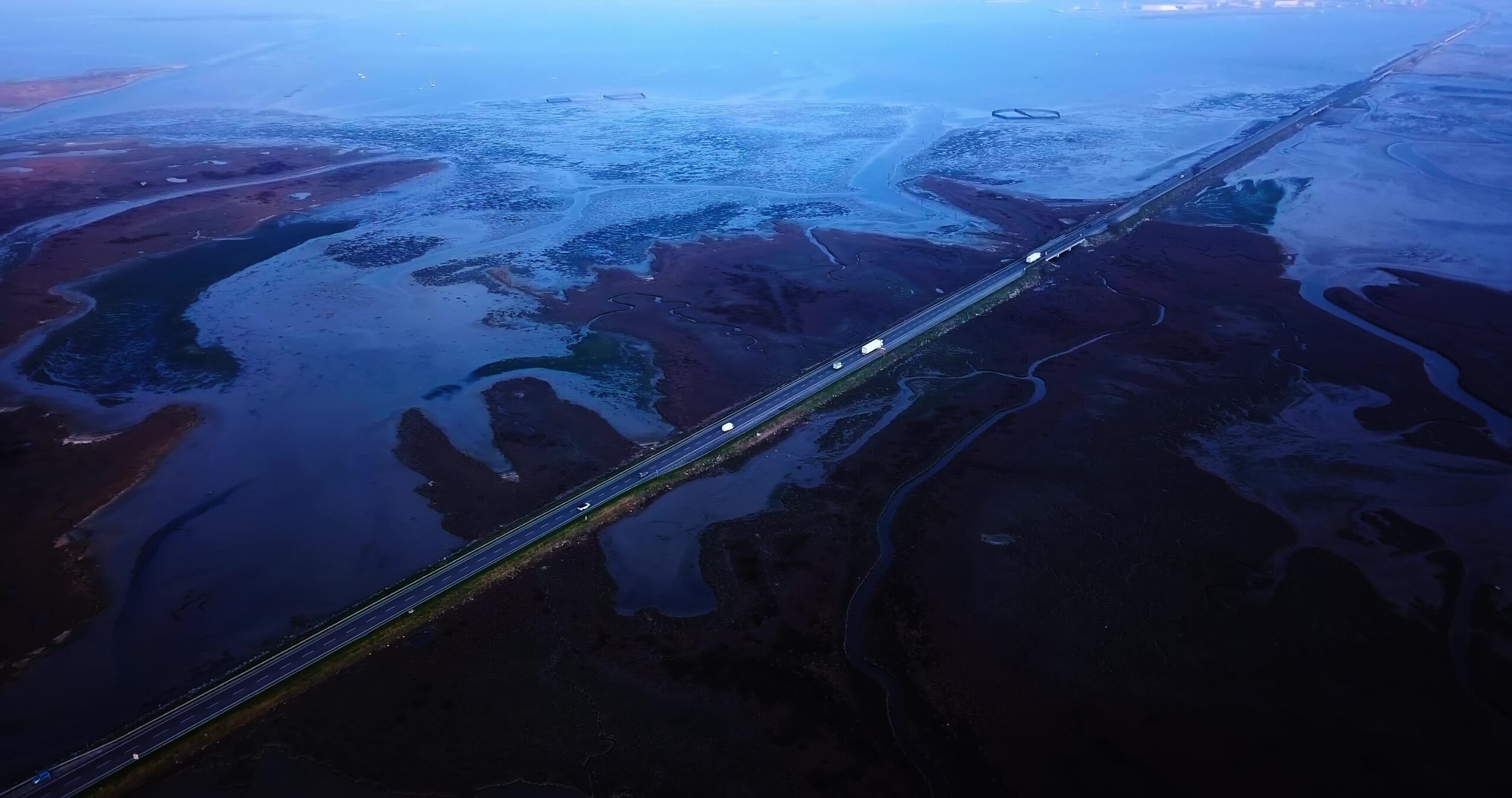 Cars drive on highway among vast Venetian lagoon at night