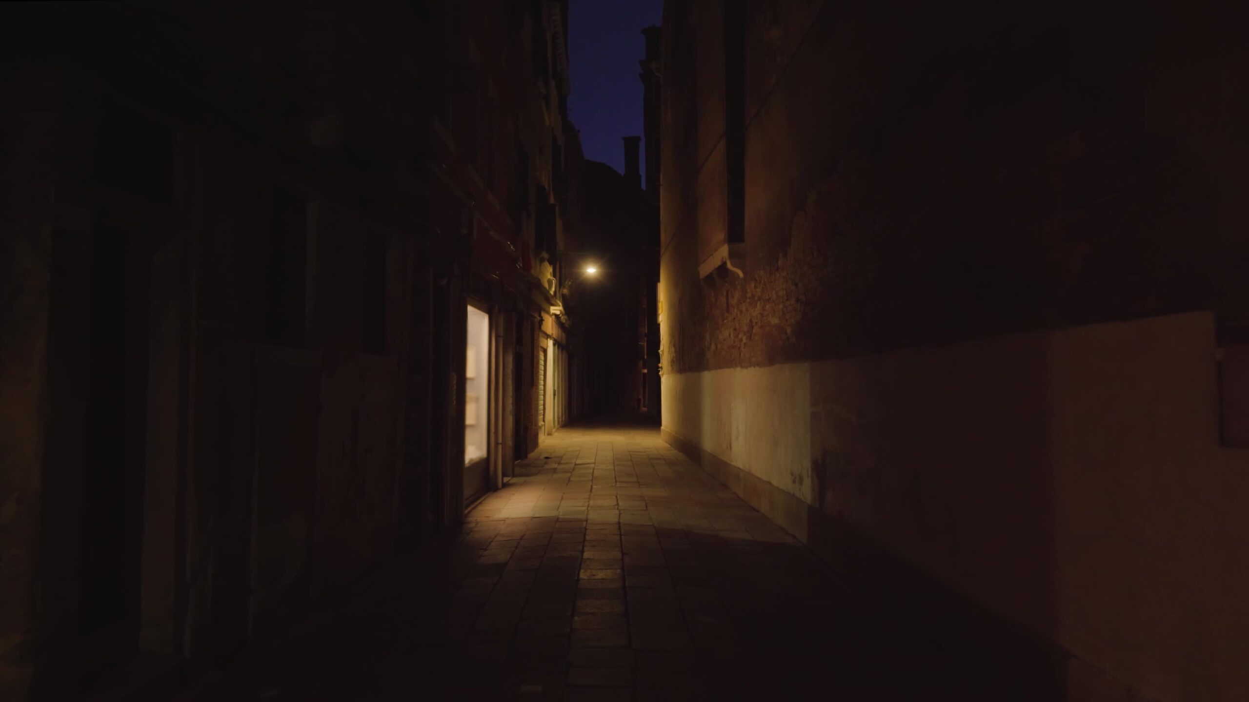 Long narrow dark empty street illuminated by window and lamp