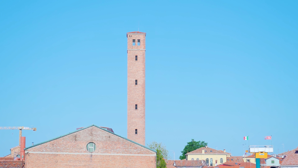 High brick tower among buildings in Murano under blue sky