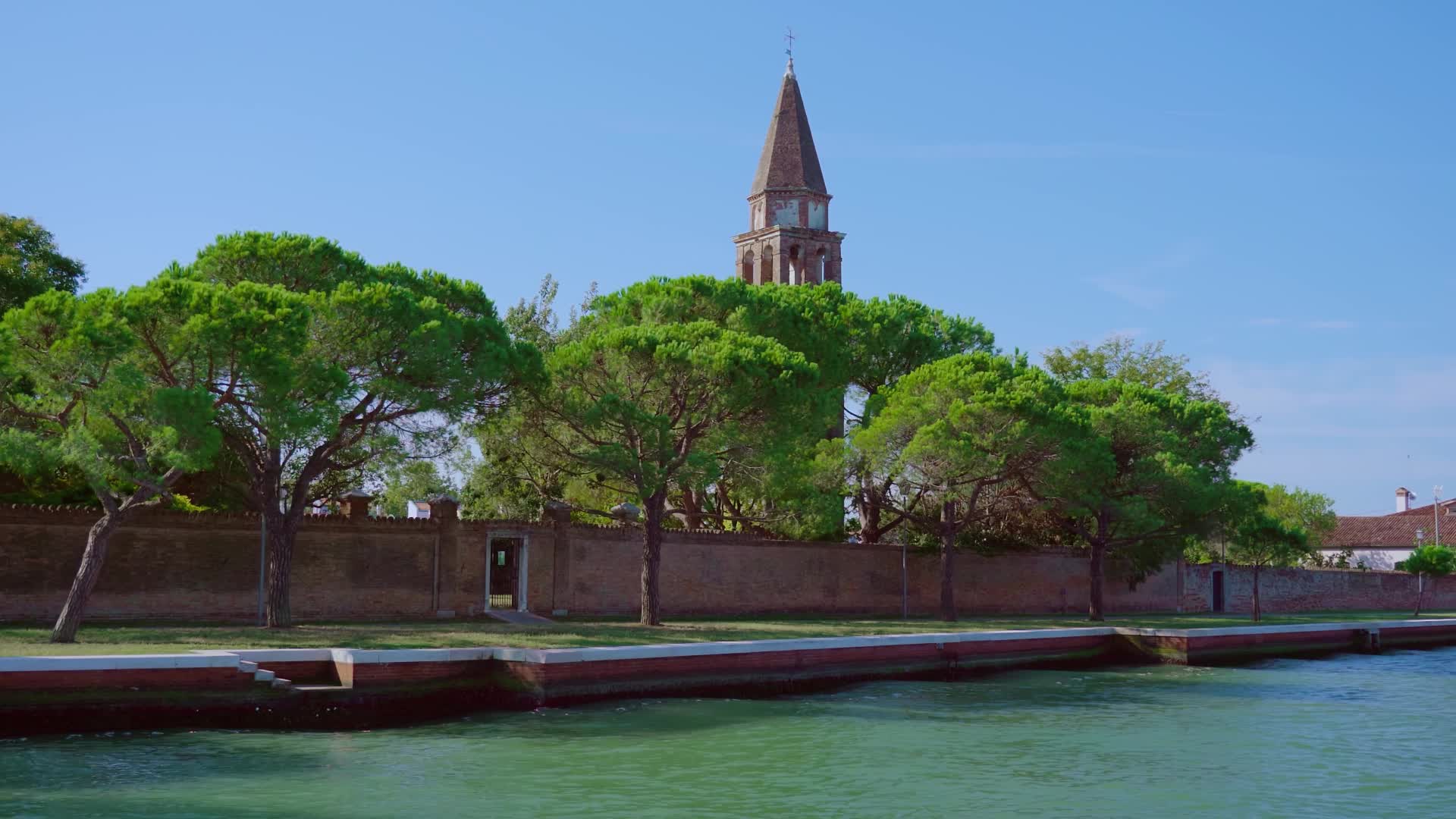 Bell tower with brick fence stands on Venice lagoon bank