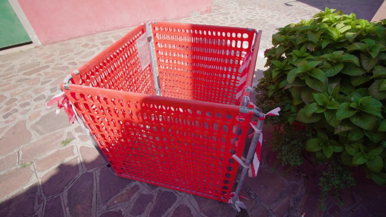 Recinzione in plastica rossa del tombino fognario nella soleggiata strada di Burano