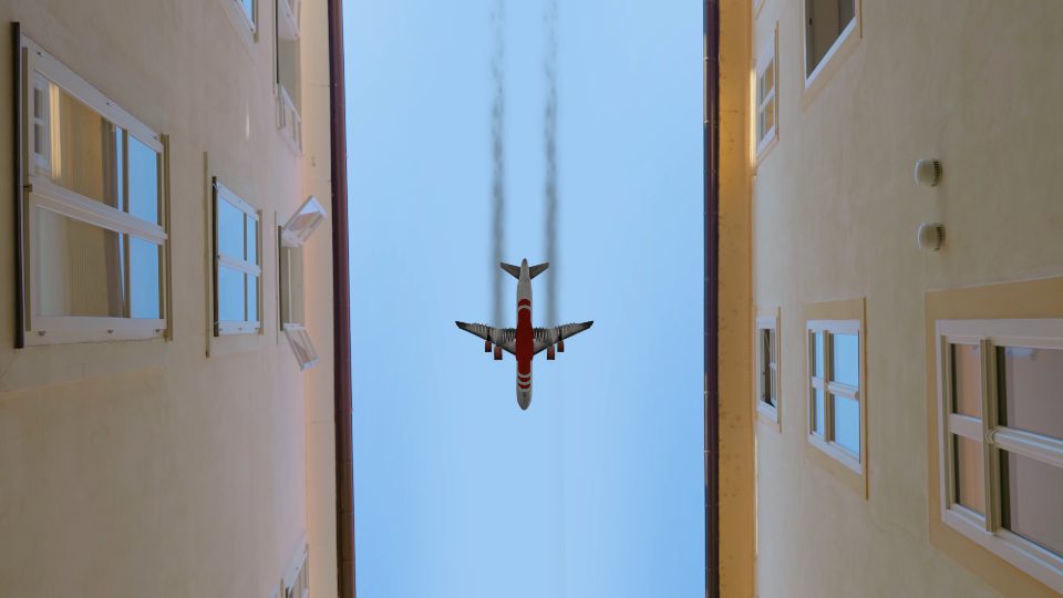 Airplane flies between buildings against blue sky in city