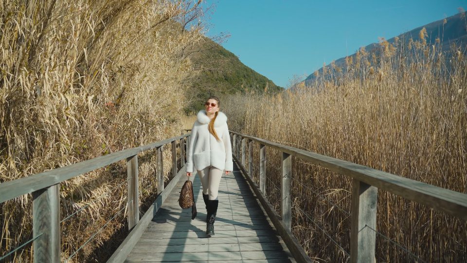 Young stylish woman walks on wooden bridge build over pond