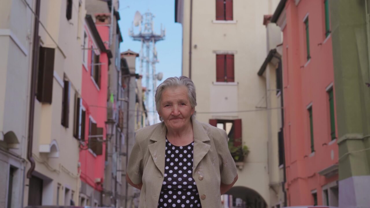 Donna  anziana dai capelli grigi cammina lungo la strada antica