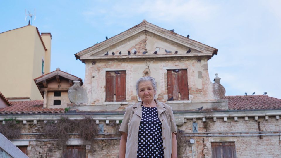 Donna anziana davanti vecchio edificio abbandonato