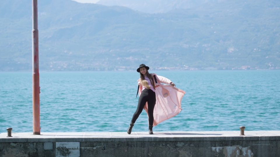 Woman enjoys dancing on pier at Lake Garda with blue water