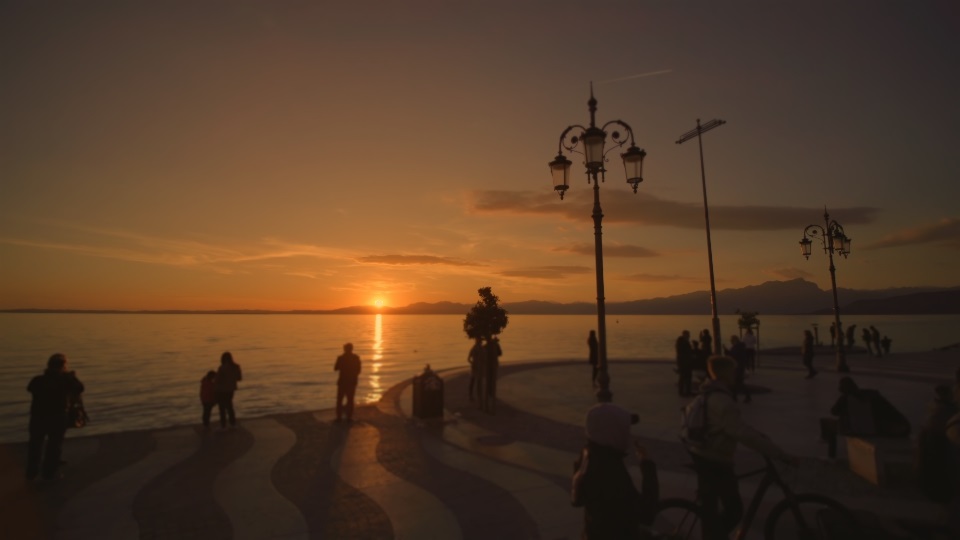 Tourists enjoy watching sunset on city waterfront near lake