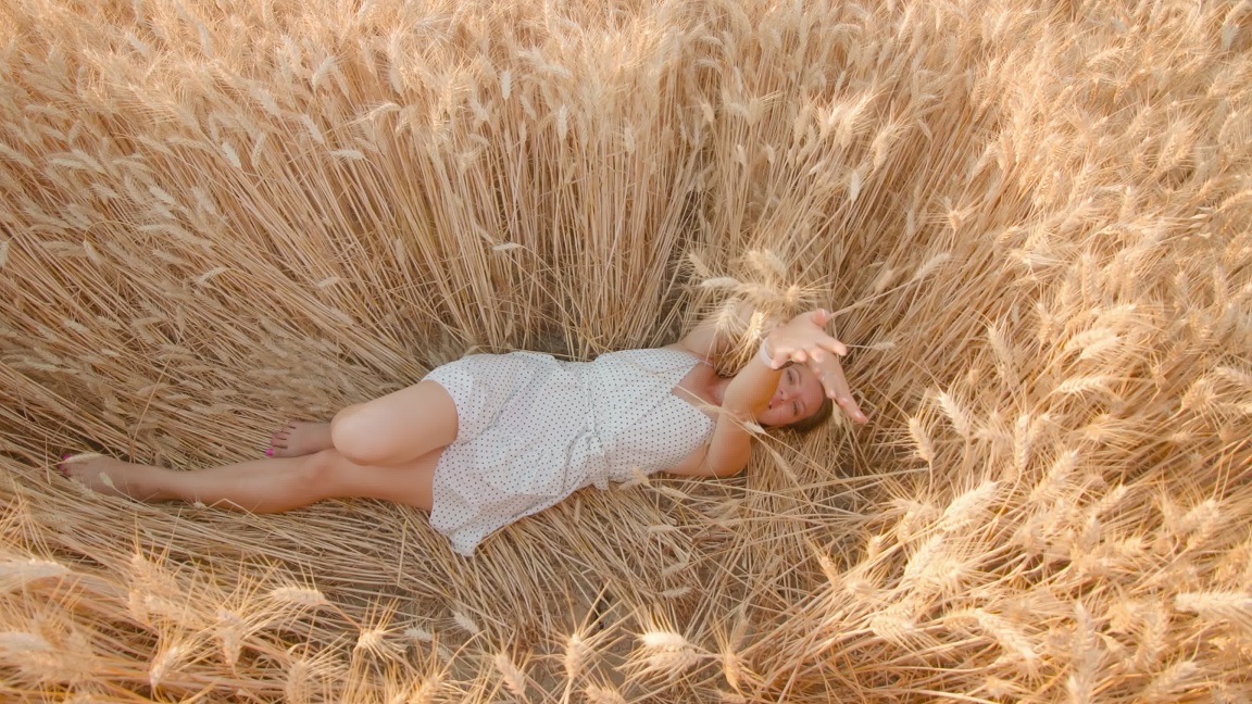 La donna si diverte sdraiata nel campo di grano dorato in una giornata di sole