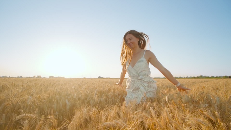 Long-haired woman enjoys running in large golden wheat field