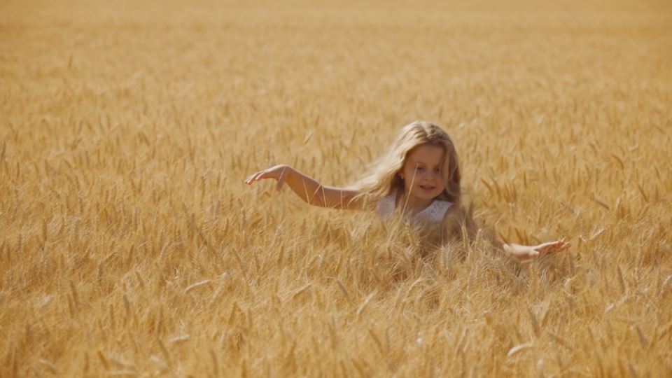 La bambina corre nel campo di grano con alte spighette dorate