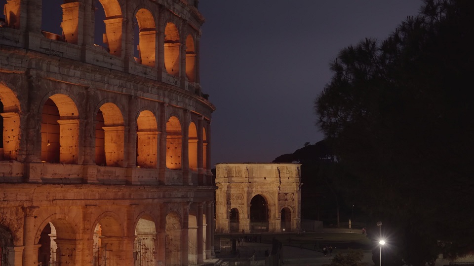 Illuminated Colosseum by triumphal arch in Rome at twilight