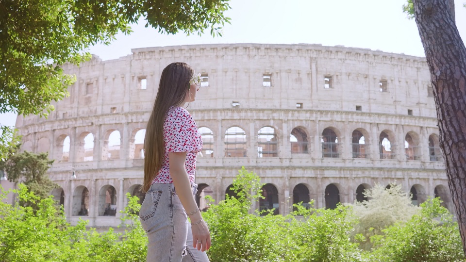 Young woman walks against large Colosseum behind trees