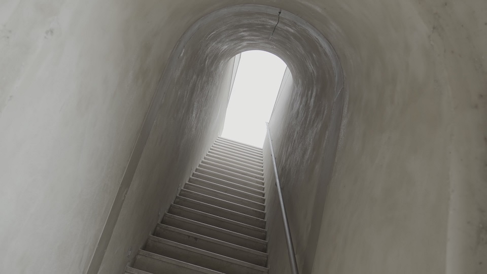 Bright light illuminates tunnel with grey walls and stairs