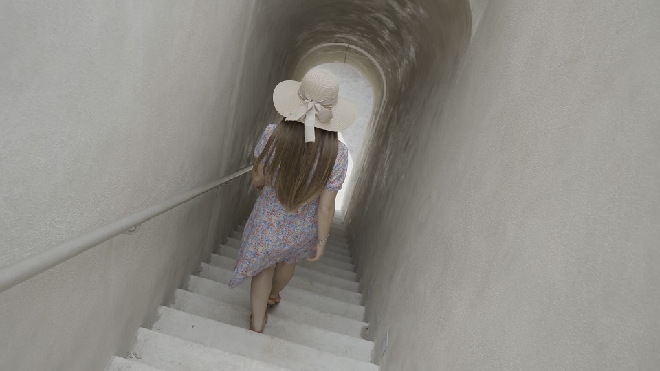 Woman in hat goes down stairs walking to exit of corridor