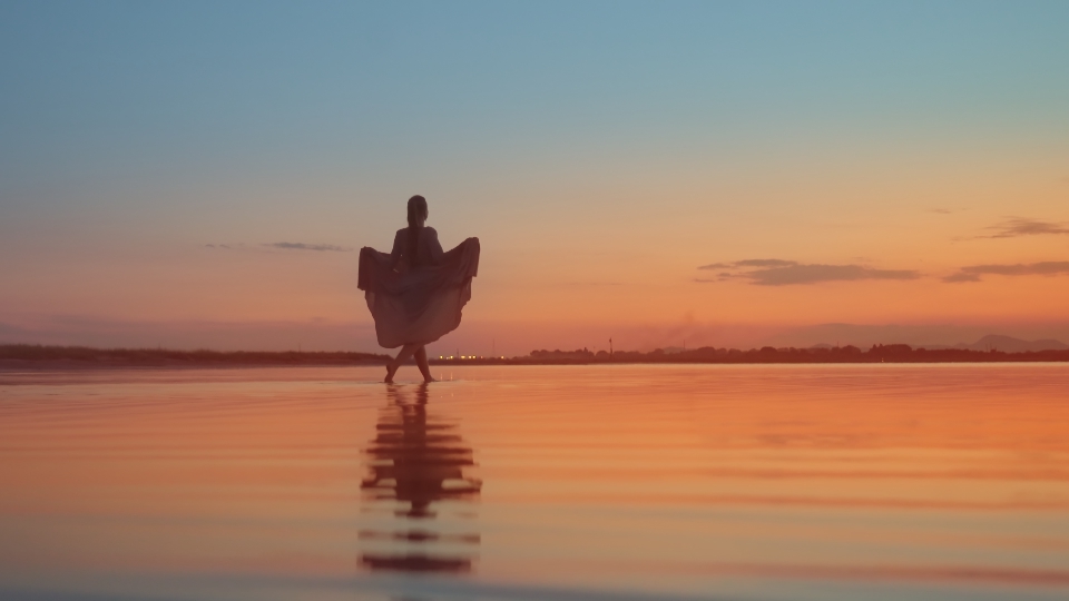 Elegant dressed woman walks on red water at sunset