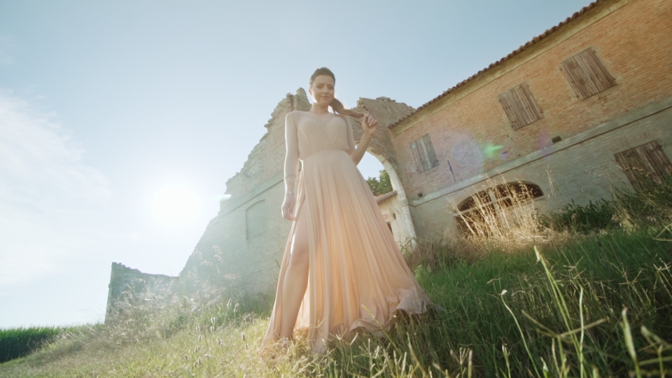 Model in elegant dress stops in front of old building