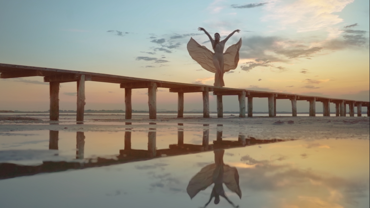 Woman’s elegant dress flies on the beach at sunset