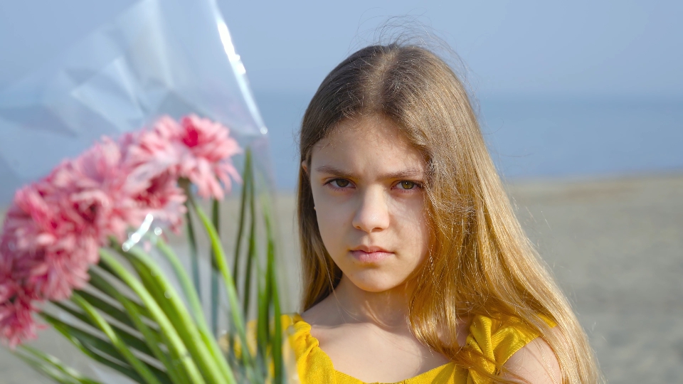 Ragazzina  tiene in mano un mazzo di fiori e guarda avanti con uno sguardo serio