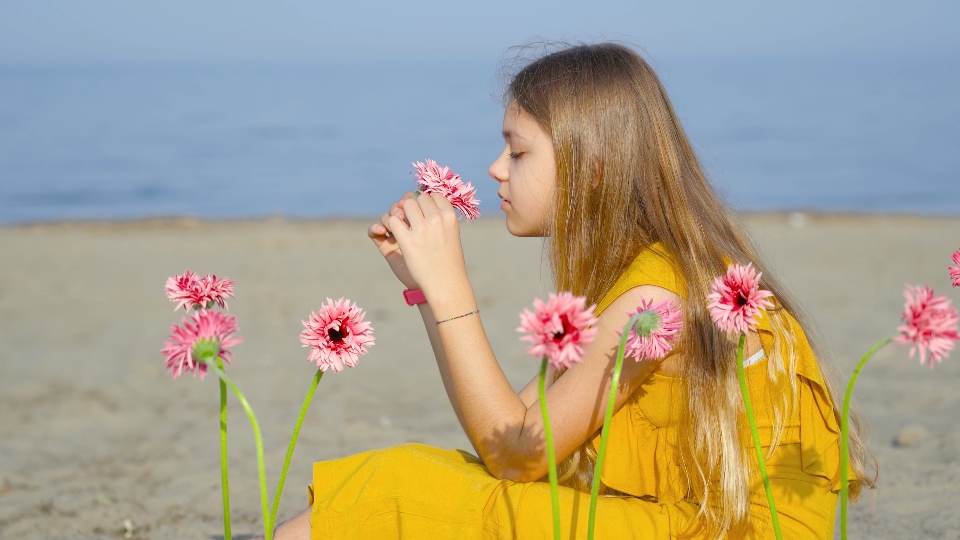 Girl dressed in yellow sitting on the beach and surrounded by flowers