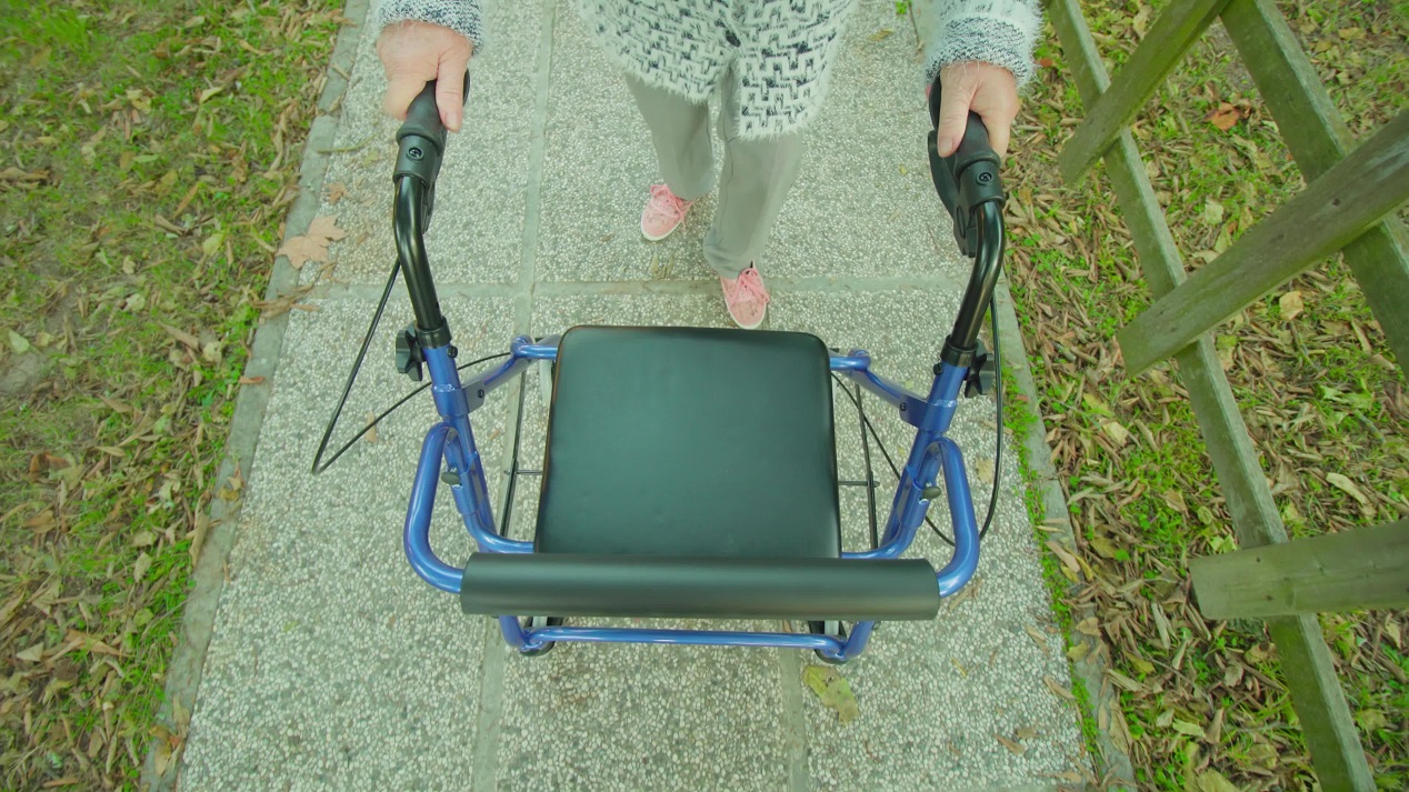 Old woman walks along cobbled park pathway with rollator