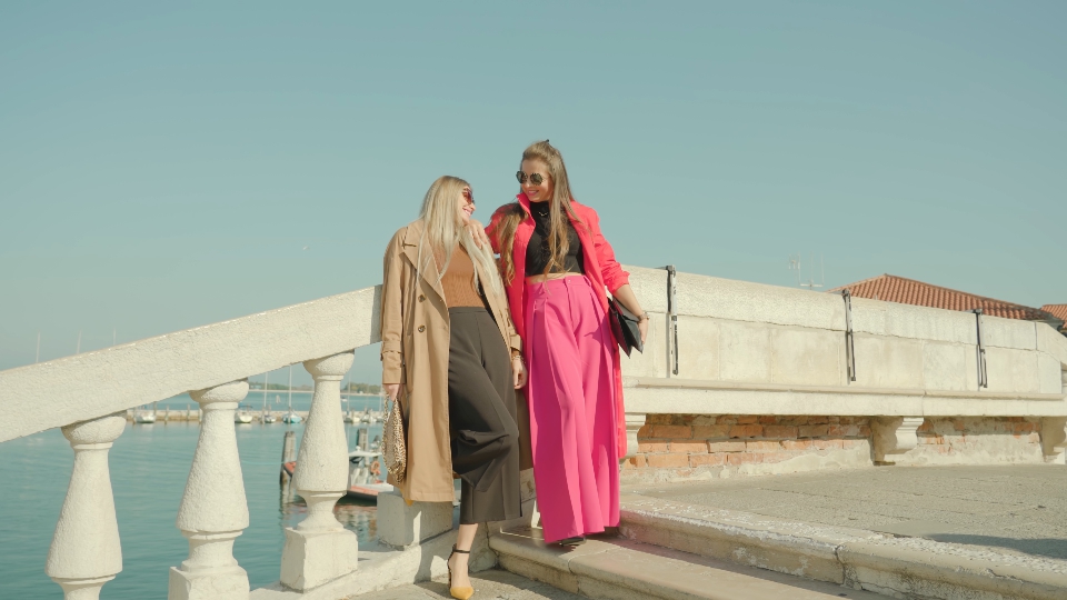 Girl friends in outfits pose on bridge over Venetian lagoon