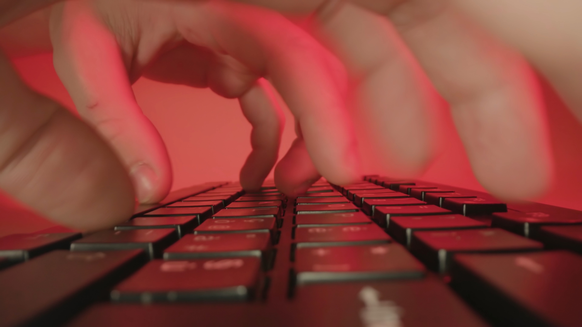 Person types fast on keyboard working at table on red