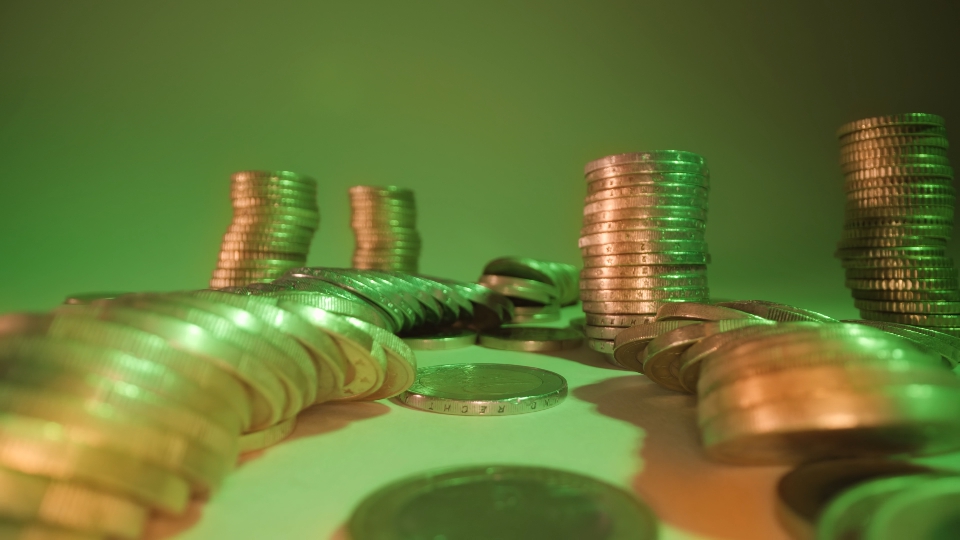 Stacks of coins fall down on table at gentle green light