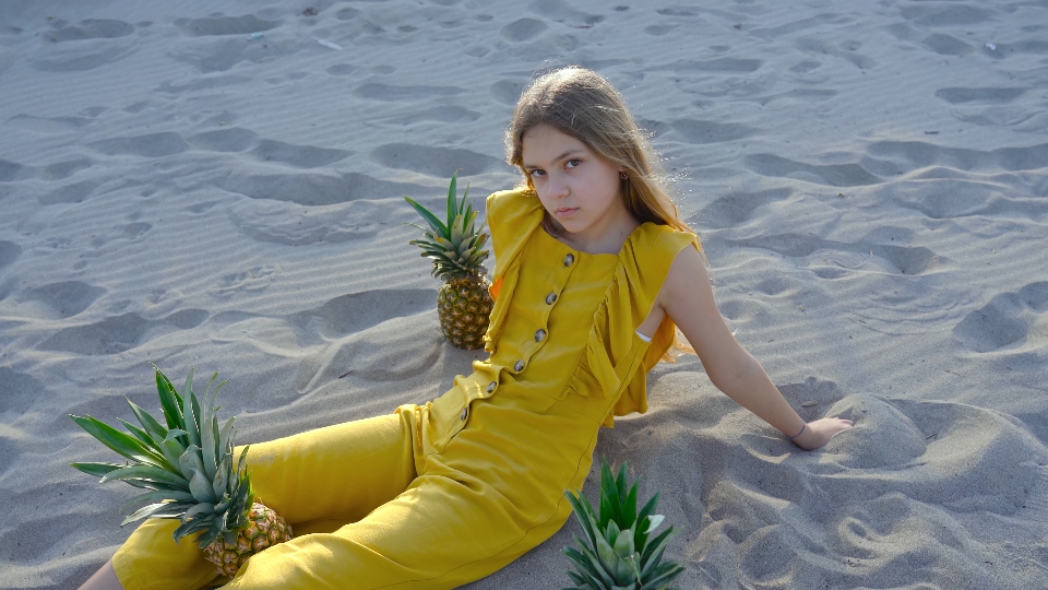 Young girl sitting on the sand with pineapple around