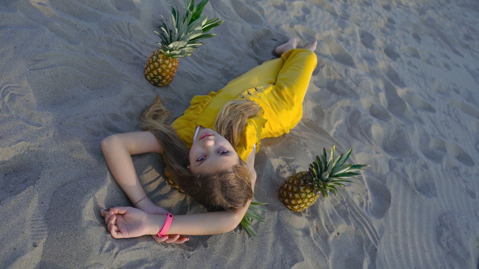 Young girl lying on the sand among the pineapples