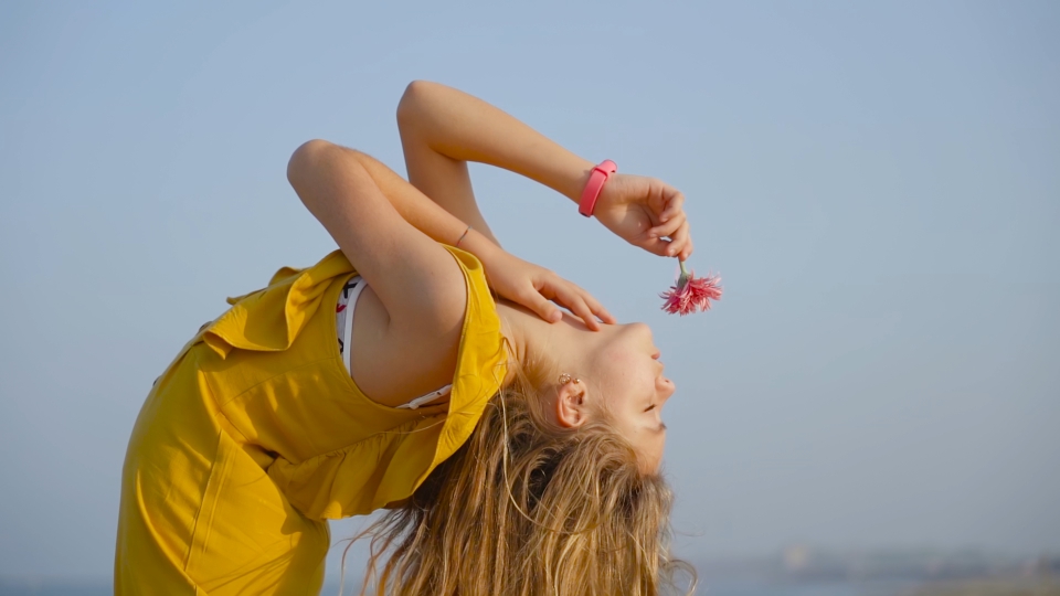 Teen bends over with a flower in her hand in slow motion