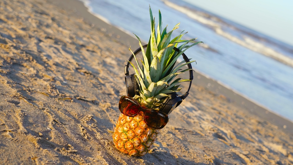 Cuffie e occhiali indossati su un ananas sulla spiaggia