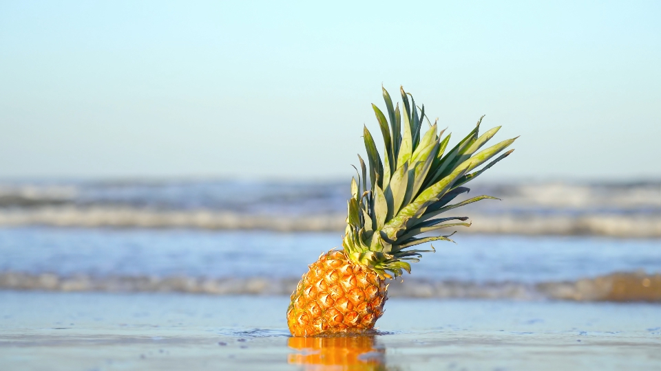 Il mare copre al rallentatore un ananas sulla sabbia