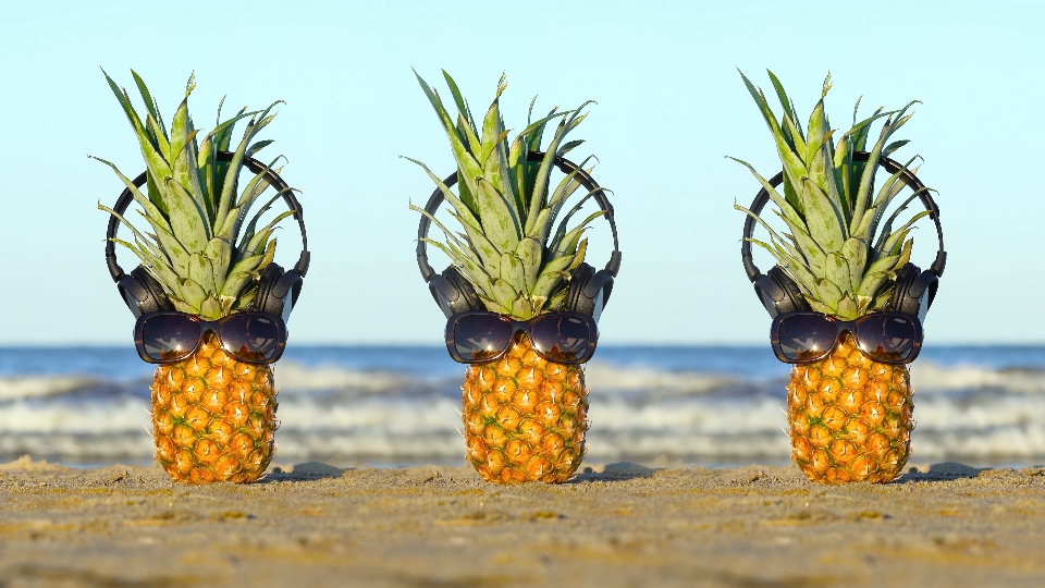 Ananas con occhiali e cuffie sulla sabbia del mare