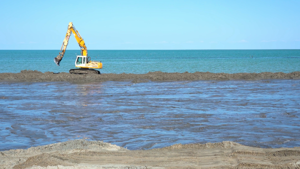 An excavator works on the sand at the beach