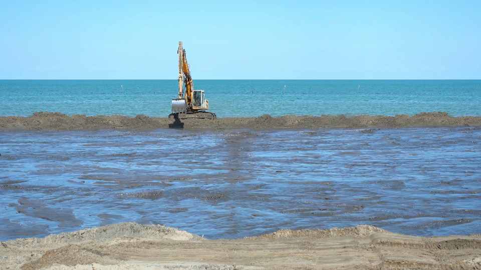 L’escavatore si sposta rapidamente ai lati del cantiere sulla spiaggia