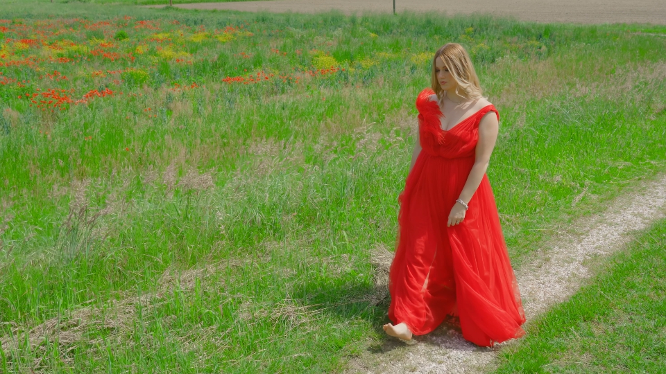 Bella donna in abito rosso elegante cammina sull’erba verde