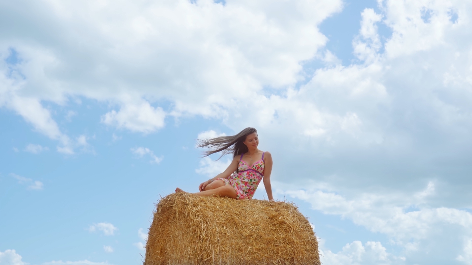 Woman sitting on bale of straw against blue sky background