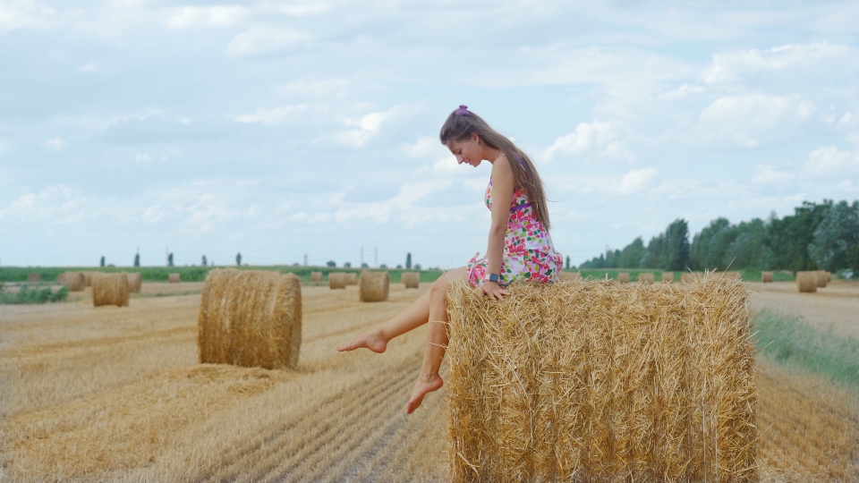 Happy woman sitting on hay bale on field