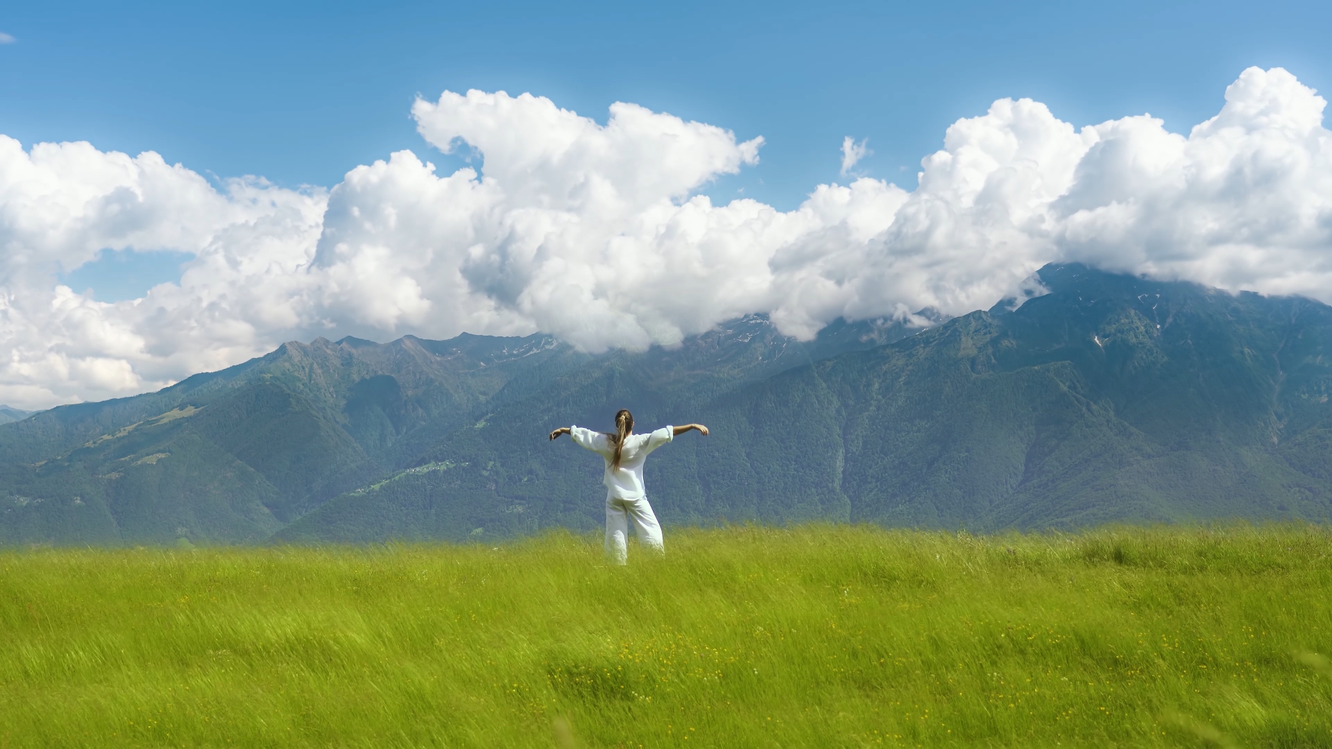 Woman relaxes with open arms in front of green mountains landscape