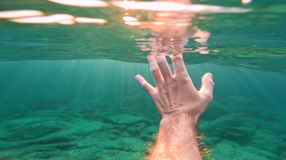 Hand underwater illuminated by sun rays