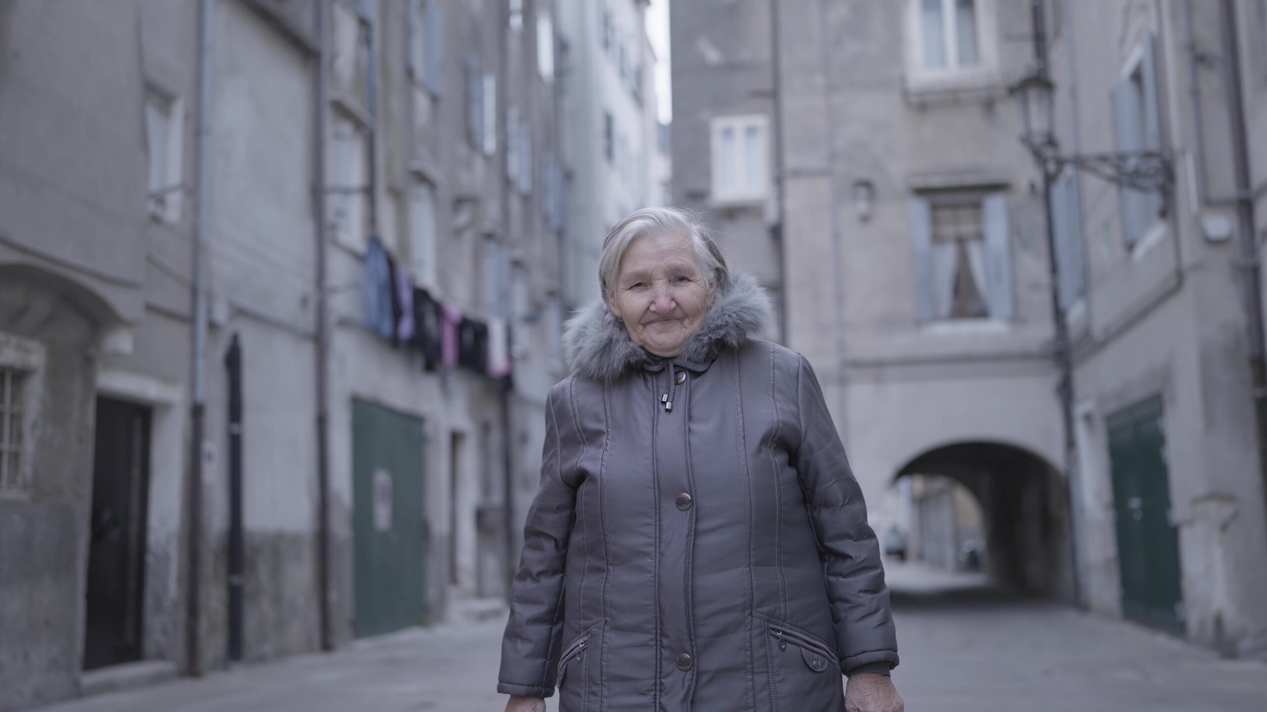 Elderly woman strolling down alley between two buildings in city